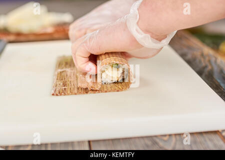 Faire cuire dans des gants jetables faire sushi roll. chef mains effectuant de longs sushi roll. célèbre la nourriture japonaise. Banque D'Images