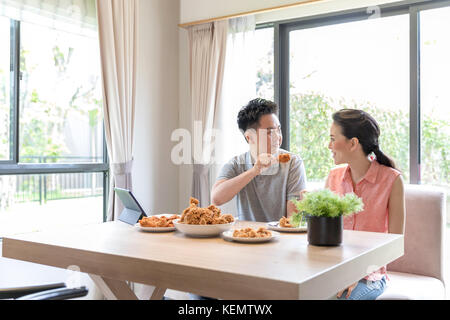 Les jeunes couples asiatique poulet frit de manger ensemble dans la salle de séjour maison contemporaine de style moderne pour concept Banque D'Images