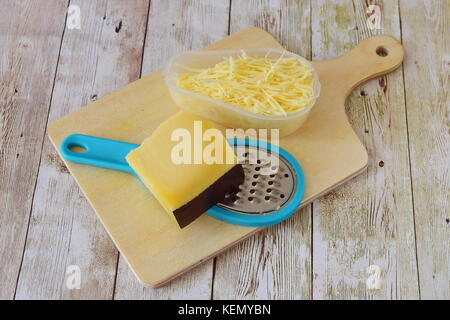 Parmesan râpé sur une râpe et un morceau de fromage de côté sur une planche à découper en bois sur un fond de bois cuisine étape par étape. Banque D'Images