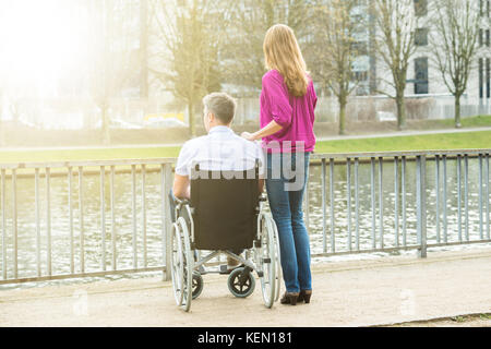 Vue arrière de la femme avec son mari handicapé sur fauteuil roulant à au lac Banque D'Images