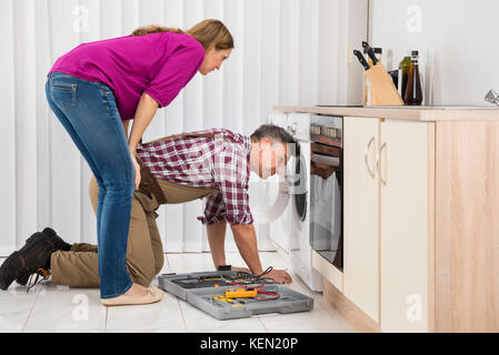 Young Woman Looking At Male Technician Réparation Lave-linge Banque D'Images