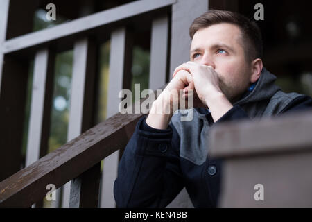 Un jeune homme est assis dans la rue et pense à des problèmes. Il est en stress permanent. C'est l'hiver Banque D'Images