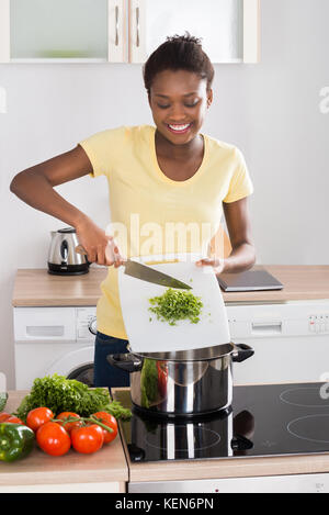 Jeune femme africaine de mettre les légumes dans le même ustensile Banque D'Images