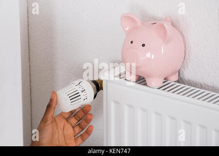 Close-up of Woman's Hand avec thermostat de réglage Tirelire sur radiateur Banque D'Images