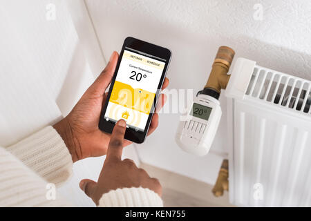 Close-up of Woman's Hand température de réglage du thermostat Using Cellphone Banque D'Images