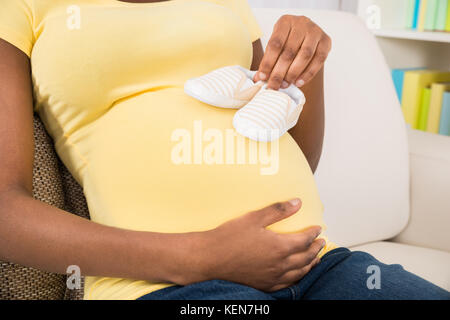 Close-up of pregnant woman Sitting on Sofa Holding Baby Shoes à la maison Banque D'Images