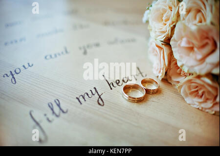 Paire de bagues de mariage dans des tons chauds, avec un bouquet des roses jaunes Banque D'Images