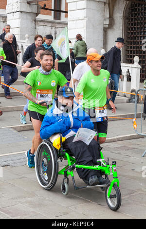 Venise, Vénétie, Italie 22 Octobre 2017. Les participants et les coureurs de marathon de Venise l'approche de la ligne d'arrivée en passant par San Marco sur le Ponte della Paglia, Groupe de qual Buon Vento avec Manuel, un jeune homme dans un fauteuil roulant. Banque D'Images