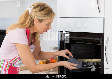 Jolie blonde woman putting tart dans le four pour la cuisson Banque D'Images