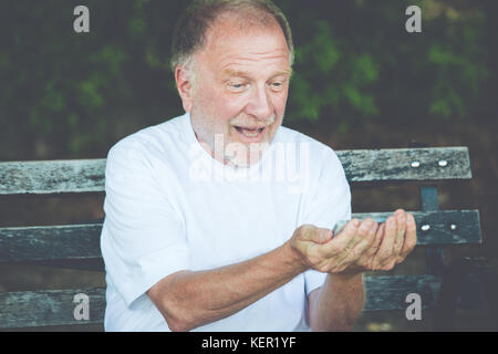 Closeup portrait of bold homme âgé en chemise blanche, excité, contrôle smartphone, l'envoi de message texte, assis sur un banc, isolé piscine backgroun Banque D'Images