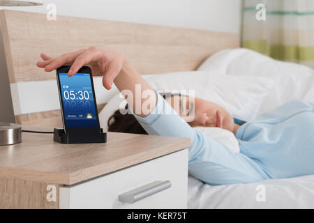 Woman lying on bed snoozing alarme sur téléphone mobile Banque D'Images