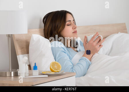 Jeune homme assis sur le lit de boire une tasse de thé dans sa chambre à coucher Banque D'Images