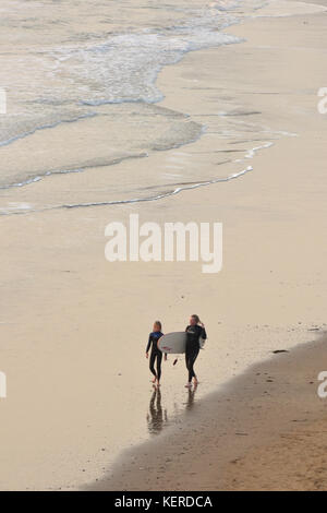 Deux jeunes gens marchant le long d'une plage de sable au bord de la mer, sur la côte dans le port d'une planche de surf surf entre leur volonté de partager le poids de ses réflexions. Banque D'Images