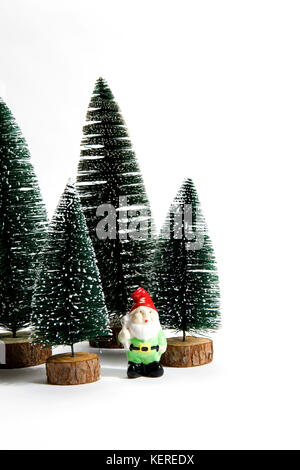 Groupe isolé de sapins artificiels complet comme une petite forêt d'arbre avec une figurine de nain de jardin à l'intérieur sur un fond blanc. photo la vie encore minime Banque D'Images