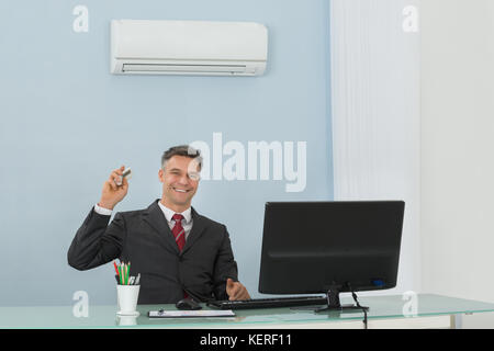 Happy mature businessman sitting on chair à l'aide de l'air conditionné dans office Banque D'Images