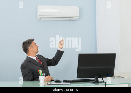 Happy mature businessman sitting on chair à l'aide de l'air conditionné dans office Banque D'Images