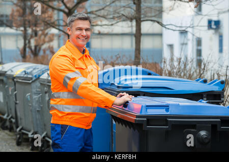 Travail heureux homme debout près de poubelle sur street Banque D'Images