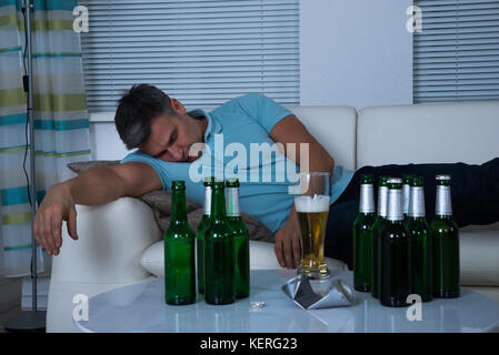 L'homme de prendre une sieste sur canapé devant des bouteilles de bière pendant la nuit Banque D'Images