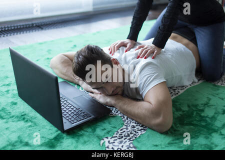Young woman giving back rub à fatigué homme étendu sur la moquette avec tablet Banque D'Images