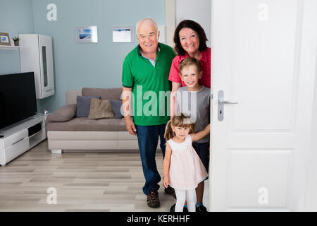 Famille heureuse avec petits-enfants debout derrière la porte ouverte à la maison Banque D'Images