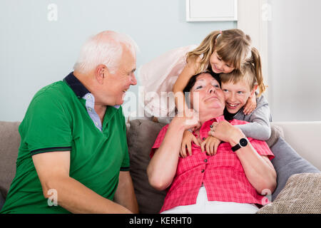 Les grands-parents âgés jouant avec ses petits-enfants sur le canapé à la maison Banque D'Images