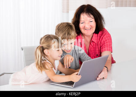 Happy Baby-sitter joue une partie avec les enfants sur l'ordinateur portable Banque D'Images