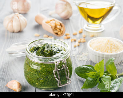 Sauce au pesto fait maison et les ingrédients sur fond de bois gris. Close up wiev de pesto de basilic dans du verre avec des ingrédients. Banque D'Images