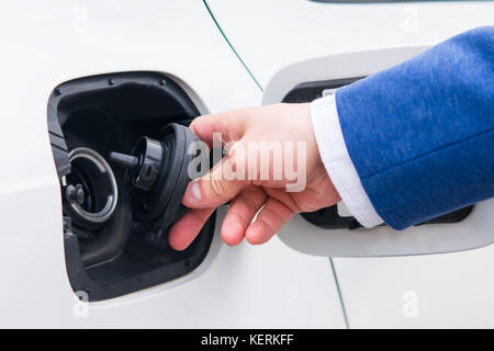 Ouvrez le couvercle du réservoir de carburant dans la voiture. Le remplissage des véhicules dans une station d'essence dans un costume d'affaires Banque D'Images