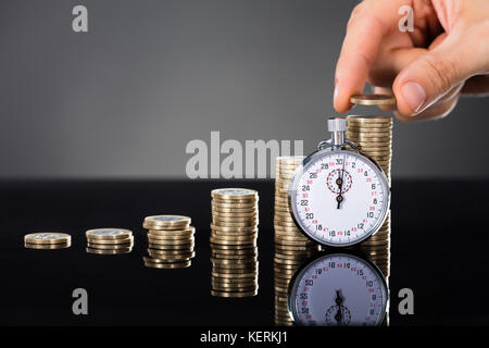 Close-up of a empiler des pièces en 24 près de chronomètre sur fond gris Banque D'Images