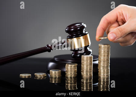 Close-up of a hand stacking coins en face de mallet sur fond gris Banque D'Images