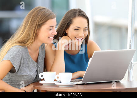 Deux amis heureux regardant le contenu diffusé en ligne dans un ordinateur portable assis dans un bar terrasse Banque D'Images