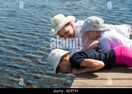 Père avec les enfants se coucher et regarder un beau lac et des poissons dans l'eau Banque D'Images