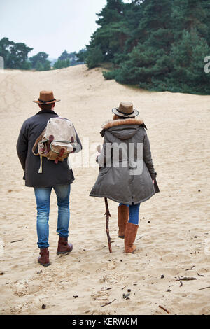 Vue arrière de young couple wearing pignon hiver randonnées à travers une zone de dunes de sable Banque D'Images