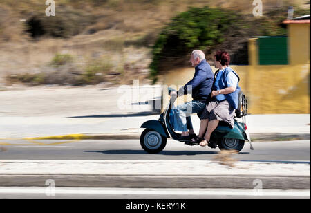 Un couple âgé, homme et femme, roulant sur un vieux scooter sur l'île de Rhodes. Aucun des deux ne porte de casque Banque D'Images