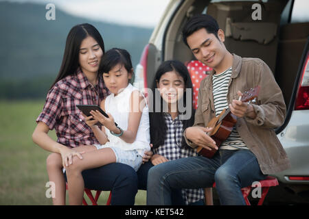 Happy little girl playing ukulele avec asian family dans la voiture pour profiter de la route et les vacances d'été dans le camping-car Banque D'Images