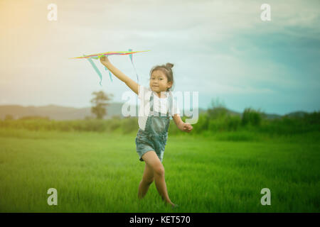 Enfant asiatique fille avec un cerf-volant en marche et heureux sur prairie en été dans la nature Banque D'Images