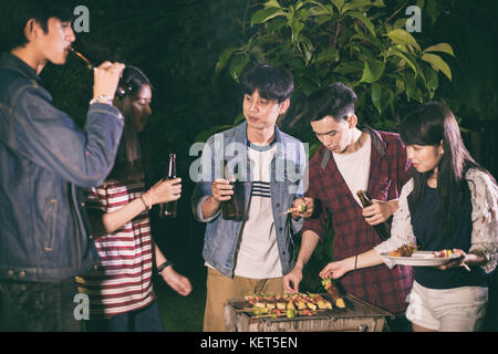 Groupe d'amis asiatiques ayant piscine jardin barbecue rire avec bière sans alcool Boissons sur nuit Banque D'Images
