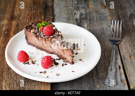 Gâteau au fromage au chocolat ou tranche de tarte à la crème au chocolat décoré avec des framboises et noix broyées sur plaque blanche. Banque D'Images