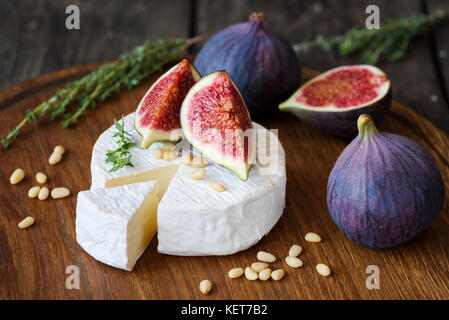 Le camembert avec des figues violettes, le thym et les noix de pin on cutting board Banque D'Images