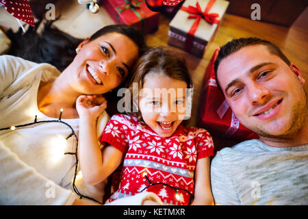 Jeune famille couché sous l'arbre de Noël chez les présente. Banque D'Images