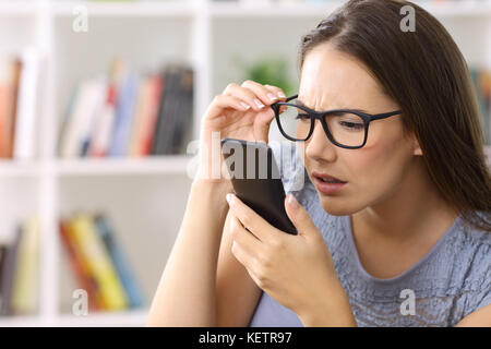 Jeune fille portant des lunettes avec des problèmes de la vue d'essayer de lire le texte à la maison de téléphone Banque D'Images