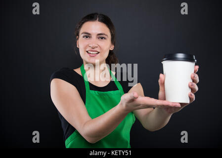 Heureux jeune vendeur offrant un café jetables à la friendly sur fond sombre Banque D'Images