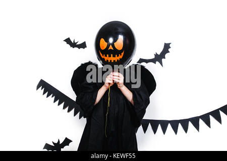 Garçon vêtu comme un ange tenant un ballon noir en face de son visage. Banque D'Images
