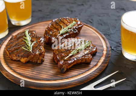 Très délicieux steak bbq et de la bière dans des verres sur une pierre noire fond. foi de savoureux steaks grillés au romarin et à la bière sur un sanglier coupe Banque D'Images