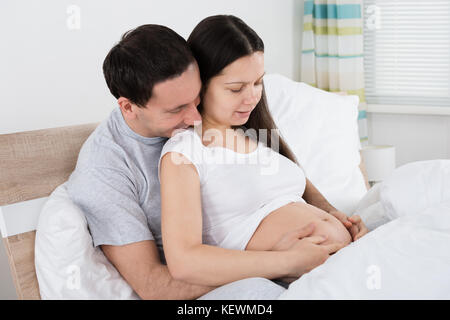 Expecting couple sitting on sofa in living room Banque D'Images