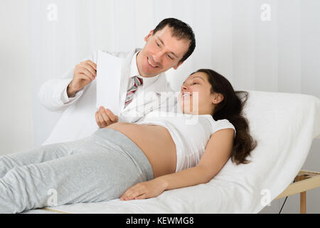 Médecin homme montrant échographie de femme enceinte en clinique Banque D'Images