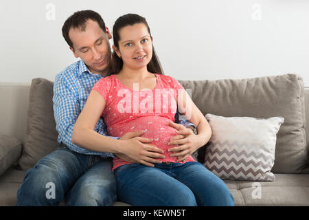 Portrait of happy young pregnant woman sitting on sofa Banque D'Images