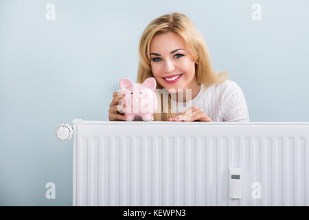 Jeune femme heureuse avec tirelire sur radiateur à la maison Banque D'Images