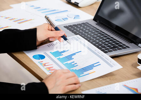 Gros plan d'Une femme d'affaires analysant un graphique avec un ordinateur portable sur un bureau en bois Banque D'Images