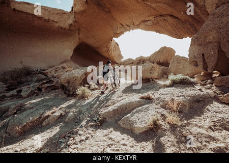 Homme marchant dans le désert avec son vtt vers rock arch, Tenerife, Canaries, Espagne Banque D'Images